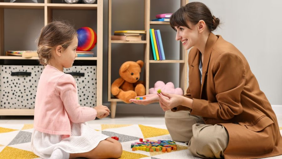 Psicóloga brincando com uma criança no chão de uma sala com brinquedos