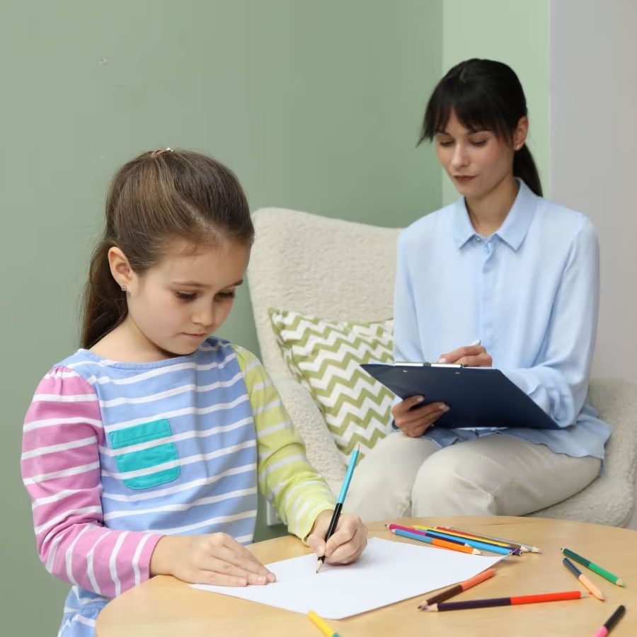 Menina desenhando enquanto a psicóloga observa e faz anotações